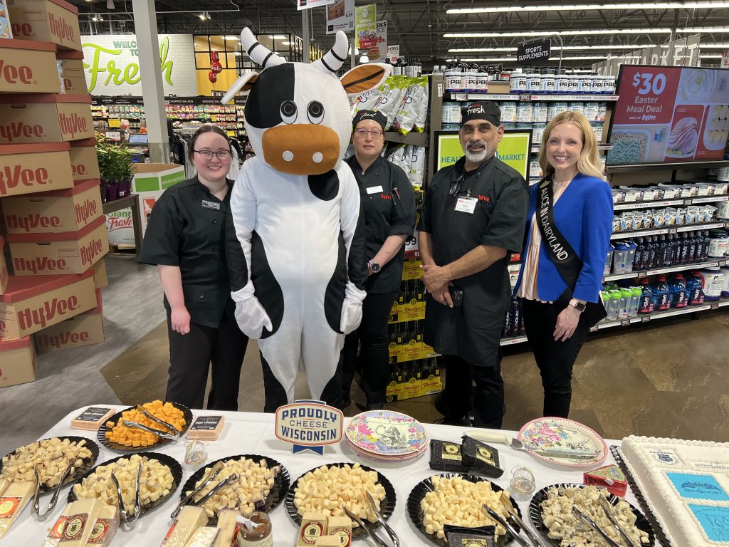 Alice in Dairyland poses with Hy-Vee employees while showcasing a variety of cheese samples.